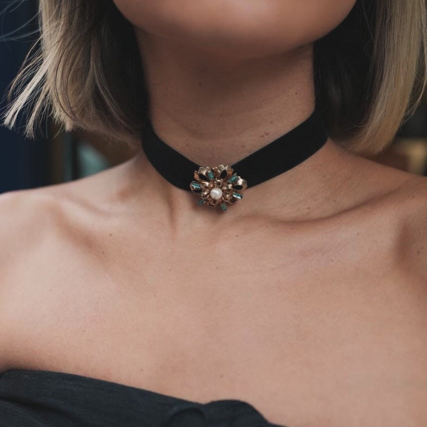 A close-up of a model wearing a black velvet choker necklace with a decorative crystal brooch at the center.